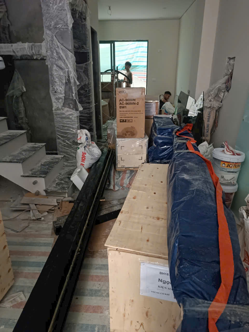 Thang máy gia đình đang lắp đặt trong nhà mới xây với thùng gỗ và thiết bị đóng gói xung quanh